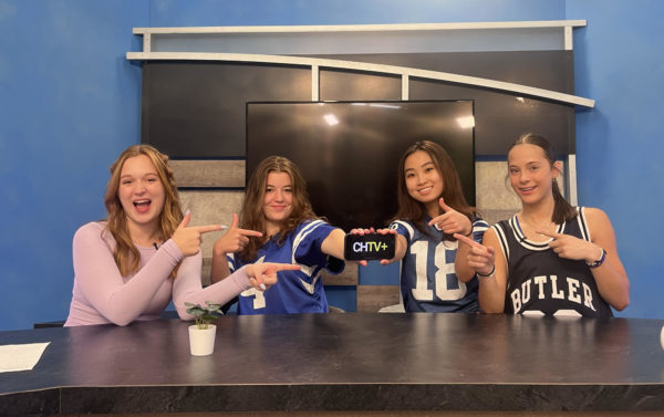 Selah, Gigi, Rebecca, and Brenna sitting at the news desk while holding a phone. On the phone is the CHTV+ logo.