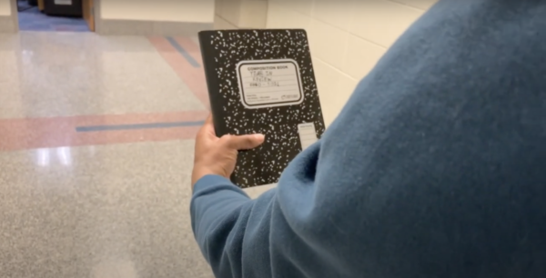 A person holding up a notebook that says, Year in Review 2020-2021