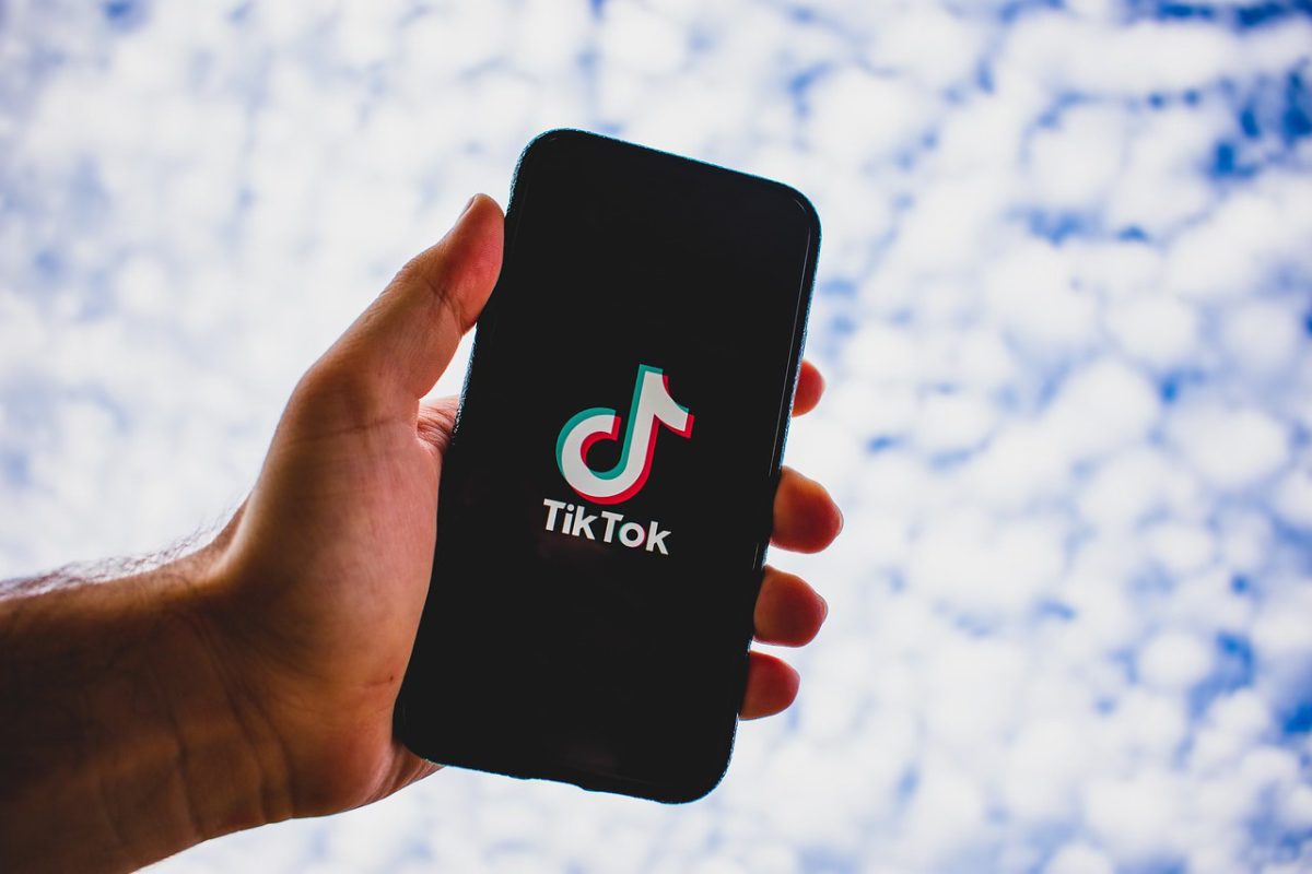 A person holding a phone. On the phone is the the TikTok logo.