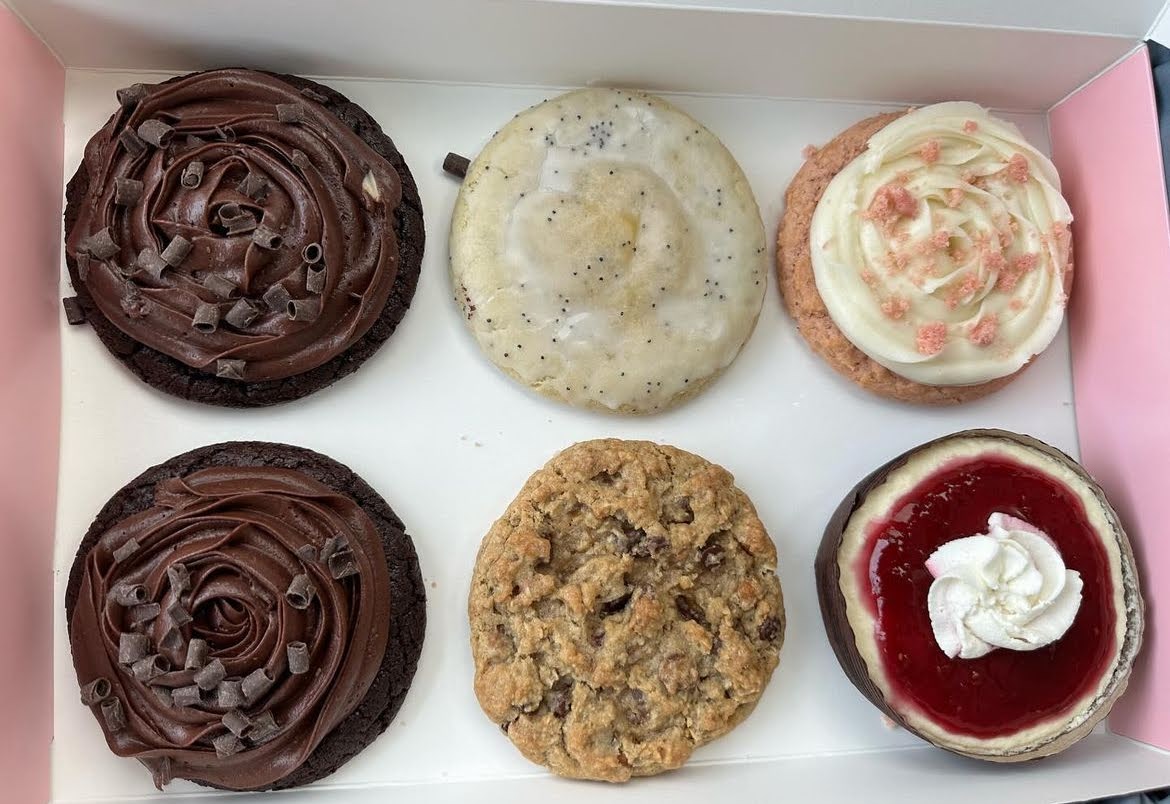 Six Crumbl Cookies in a box including Raspberry Cheesecake, Pink Velvet Cake, Mom’s Recipe, Chocolate Cake, and Lemon Poppy Seed, and Milk Chocolate Chip