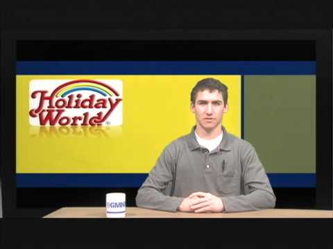 Josh Horowitz sitting at a news desk. Behind him is the Holiday World logo
