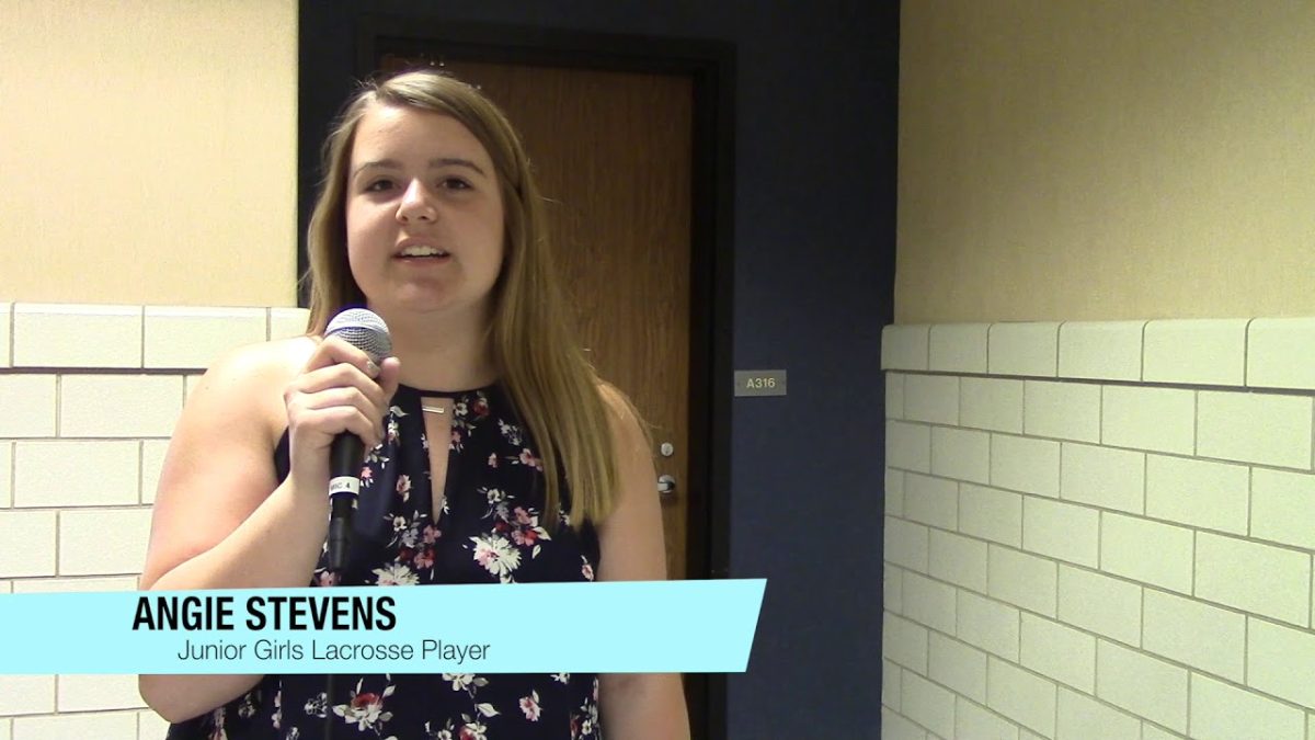 Angie Stevens standing in a hallway. In the bottom left corner of the screen, is the text, "Angie Stevens: Junior Lacrosse Player"