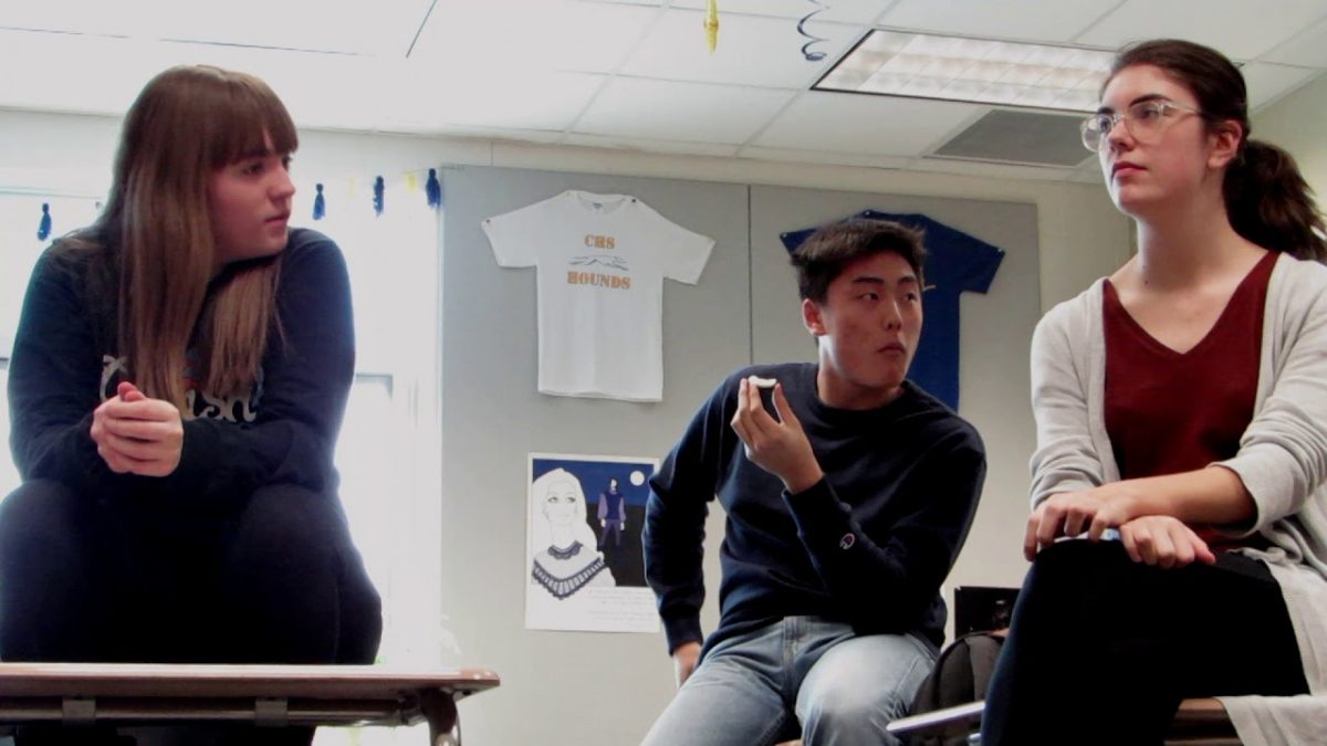 Members of the Discussion Club sitting on desks in a classroom